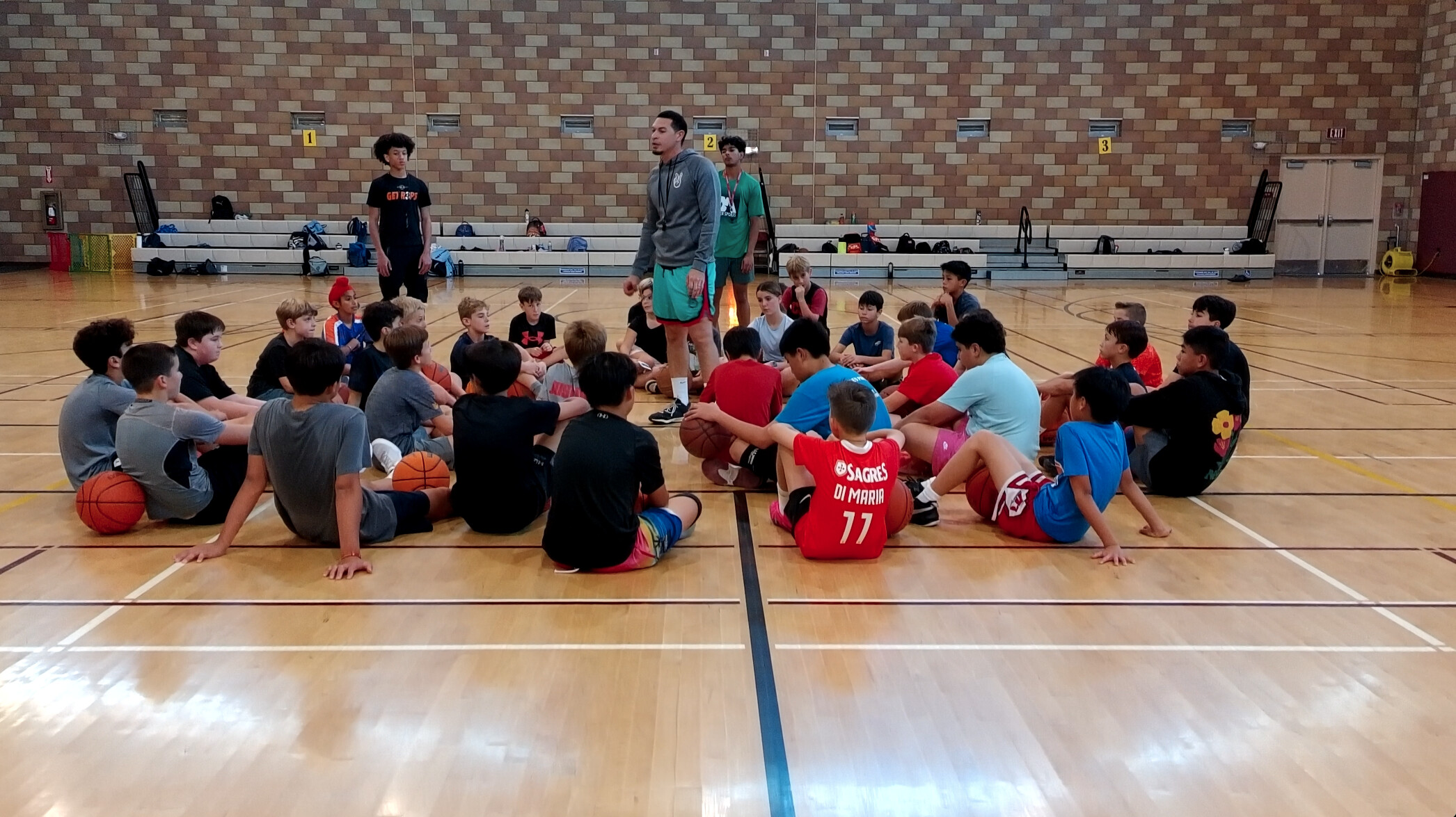 Master Sports coach speaking with young basketball players in a gym